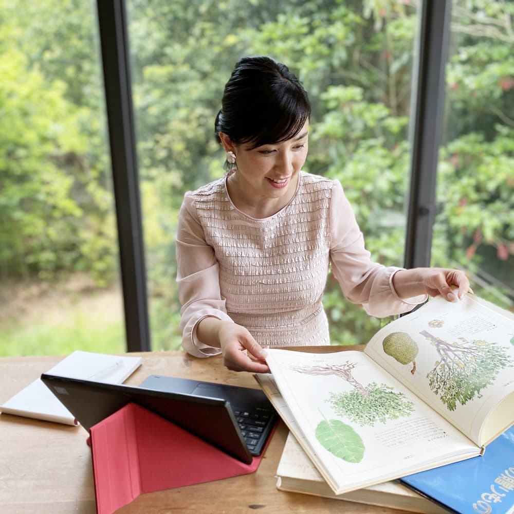 緑に囲まれて絵本を開く絵本アドバイザー小橋恵子